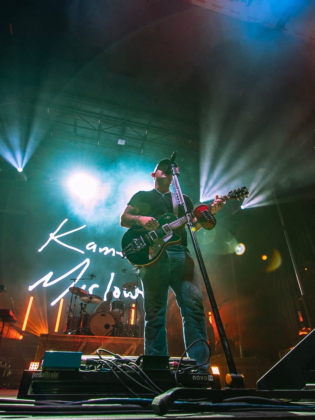A country singer with a guitar on stage under blue light at St. Pete Country Fest